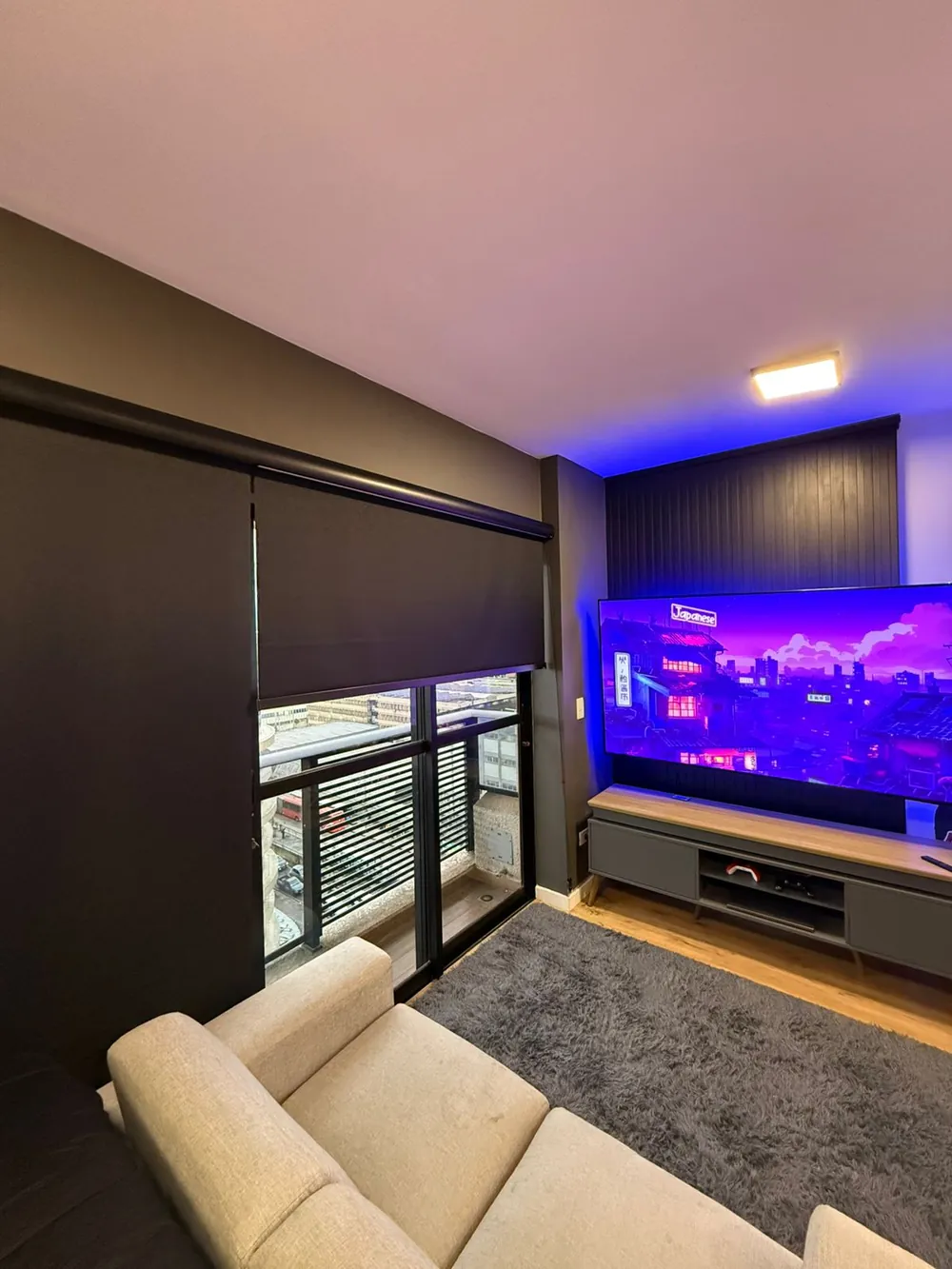 Persiana rolô blackout escura em sala com TV e porta de varanda