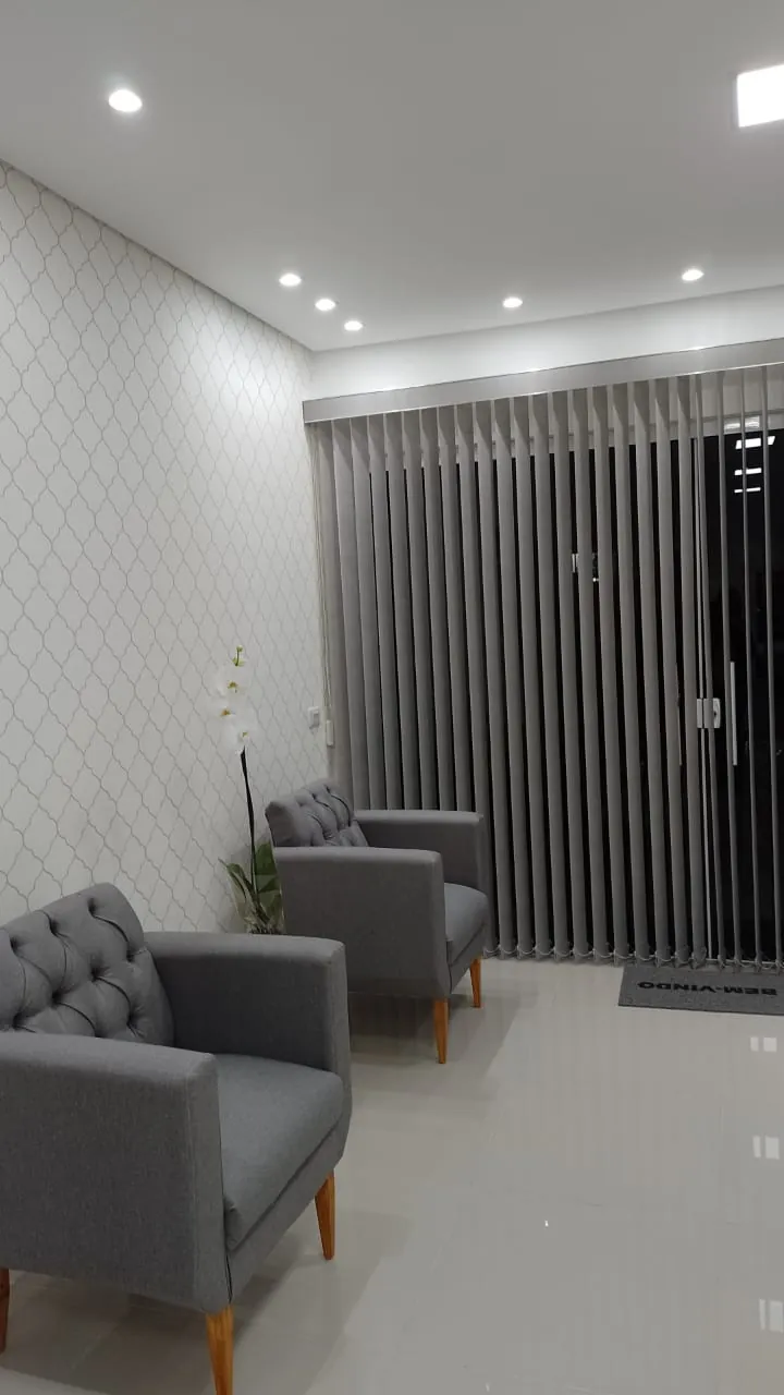 Persiana vertical cinza em porta de vidro de uma sala de espera com poltronas